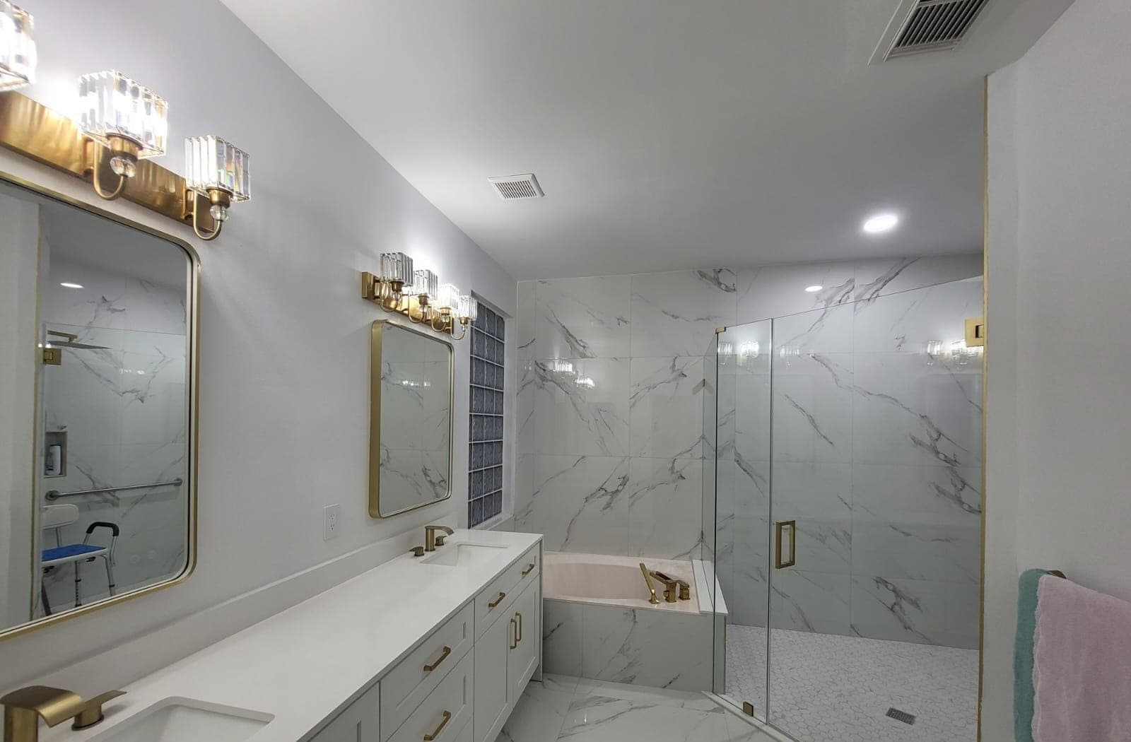 Bathroom with double vanity, gold sconces and frameless glass shower